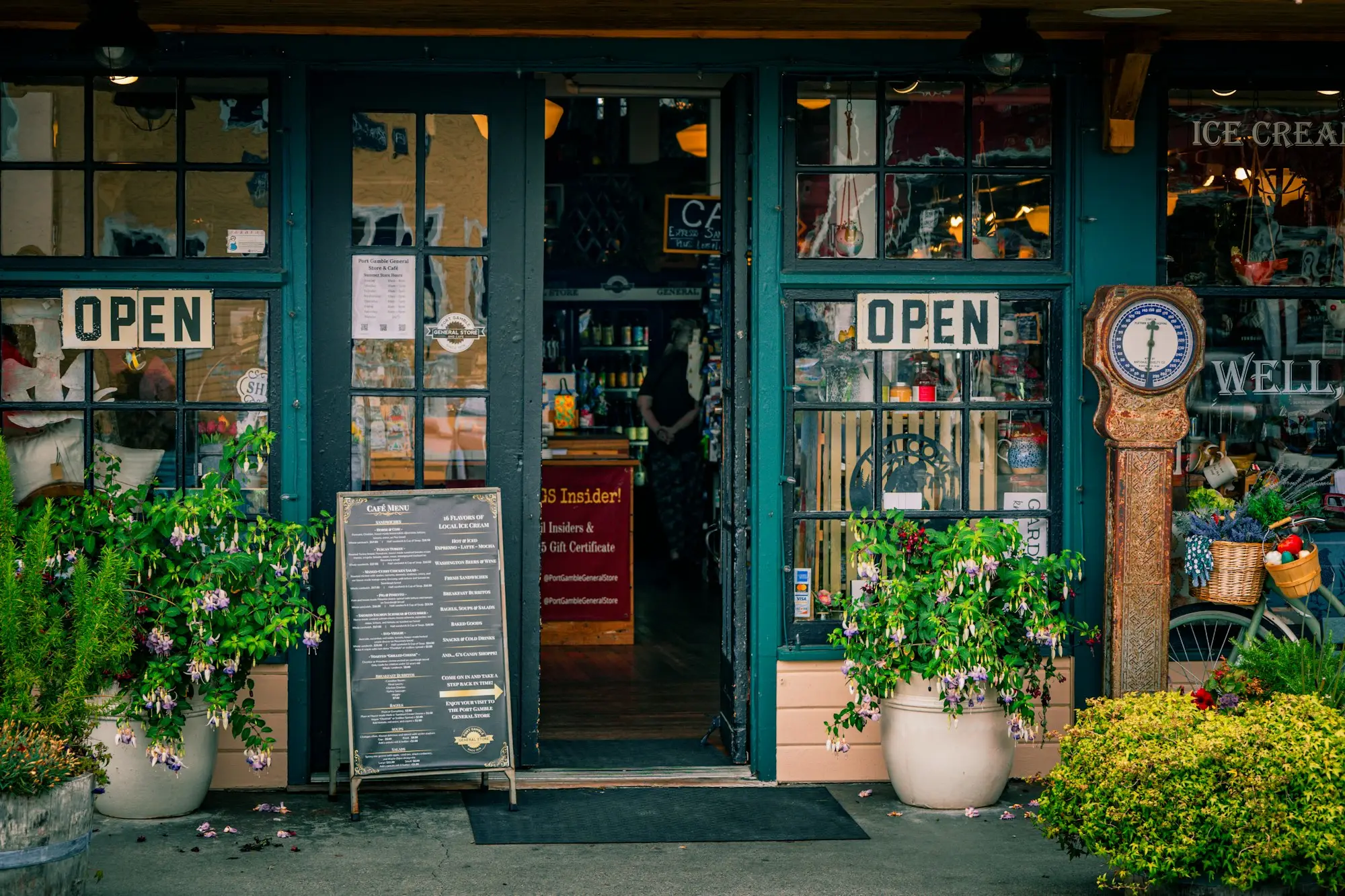 Small shopfront with open signs, flowers and a menu board at the entrance
