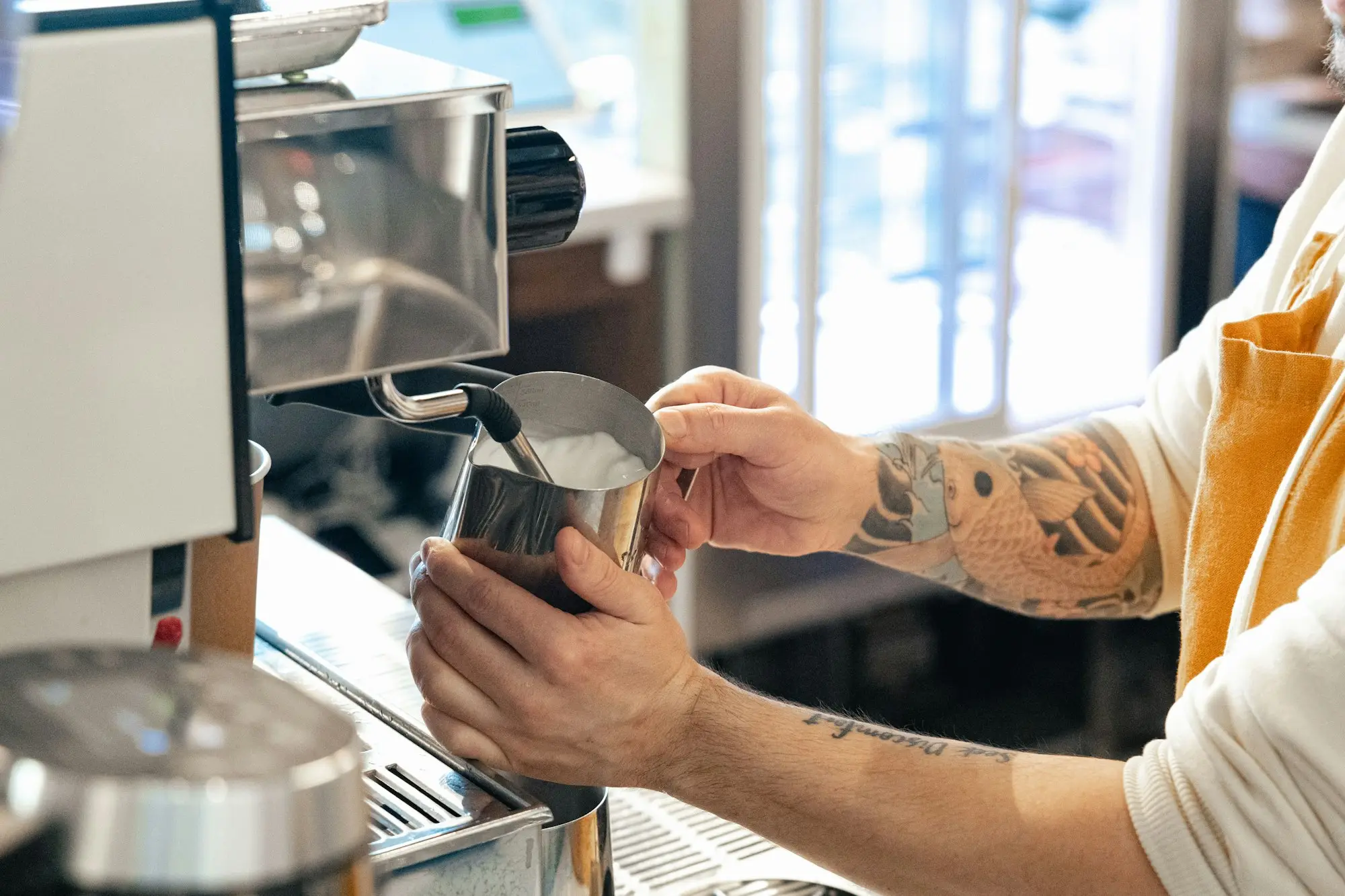 Café owner pouring milk at the espresso machine during a busy morning service