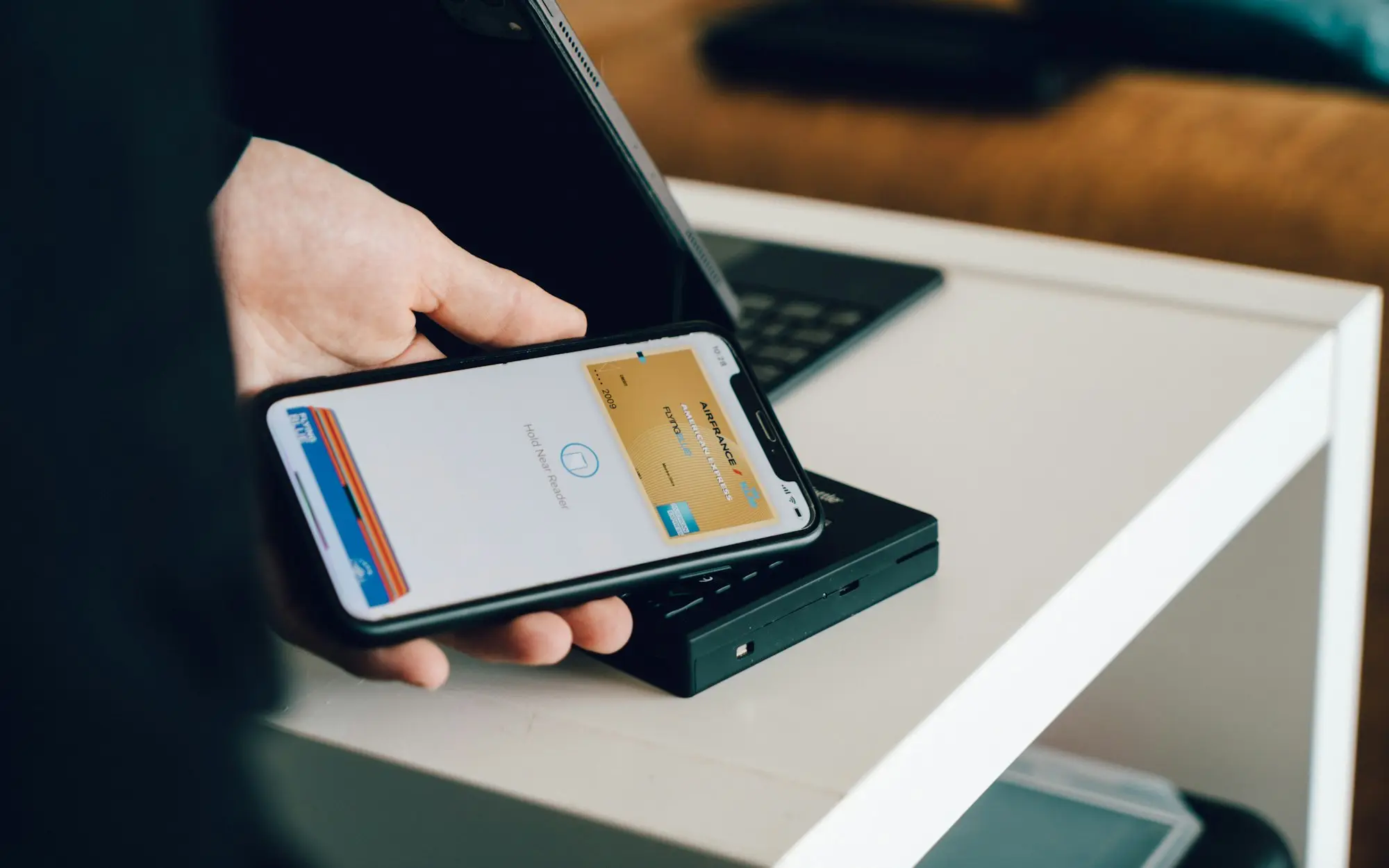 Business owner holding a smartphone over a laptop to confirm a secure online banking login